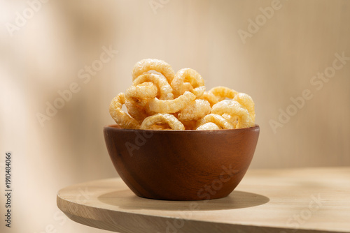 Kap Moo, crispy Thai pork rinds served in a wooden bowl on a light table. Traditional Thai snack with crunchy texture, savory taste, and natural minimal background.