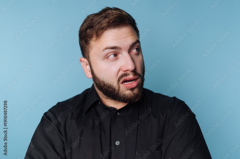 Obraz premium Surprised man reacts to unexpected news while standing against a blue backdrop