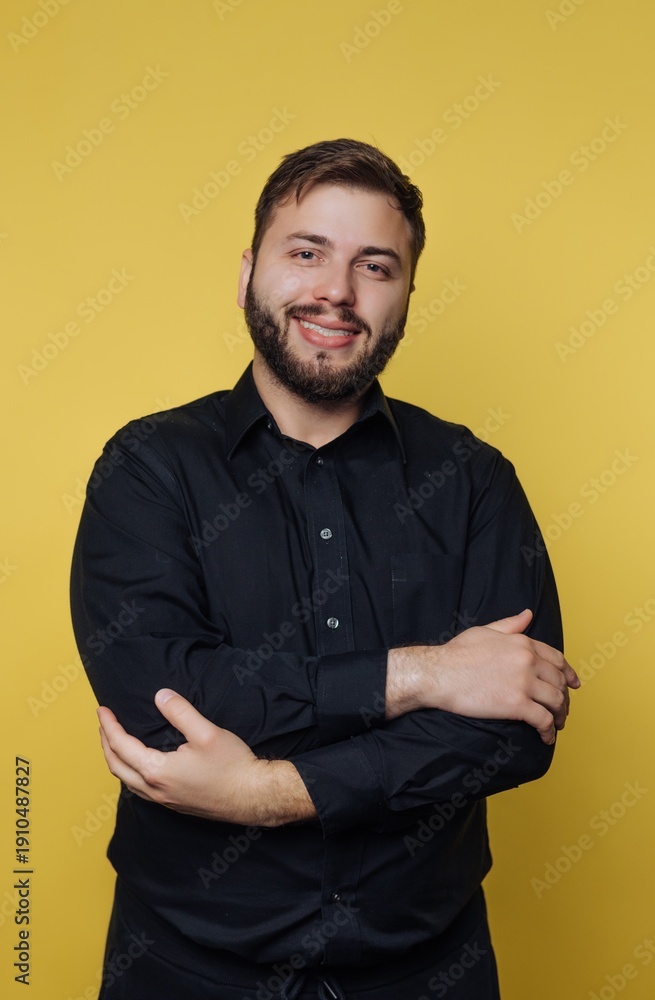 Fototapeta premium Young man with a friendly smile poses confidently against a bright yellow background while wearing a stylish black shirt