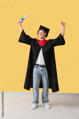Happy male graduate with diploma near yellow wall