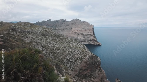 Wide panoramic movement revealing the rugged coastal cliffs and deep blue Mediterranean Sea from Mirador de Es Colomer viewpoint in Mallorca, Spain.