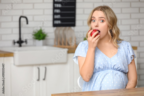 Young pregnant woman eating apple in kitchen