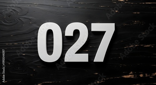 Close-up of white number 027 on black plywood with a shallow depth of field, showcasing a minimalist design with a dark, rustic background.