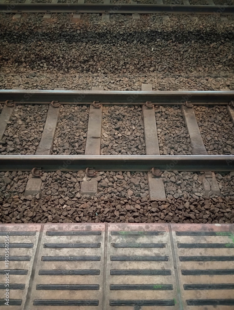 Naklejka premium Top view of railway tracks with gravel ballast and tactile paving at station platform. Transportation infrastructure and industrial background texture.