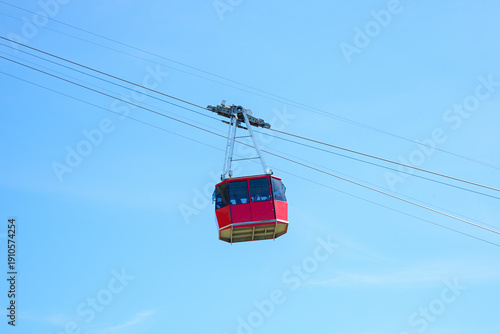 A red cable car gondola traveling upwards on a cable. Blue sky.
