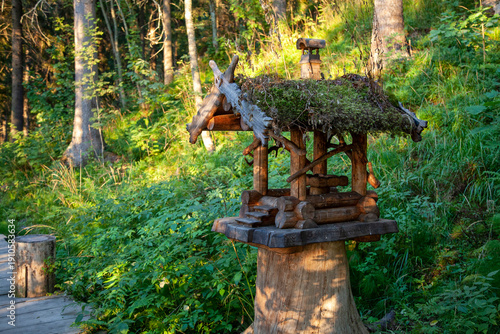 A bird feeder in the shape of a wooden house with a moss-covered roof