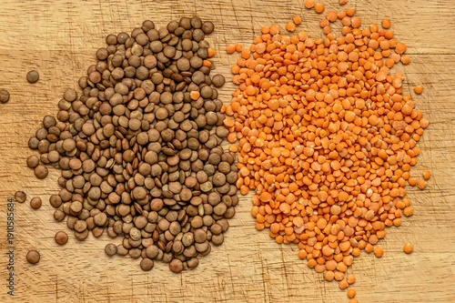 brown and red whole lentils arranged in two piles on a wooden cutting board, top view of dry legumes with natural texture, healthy plant-based food concept.