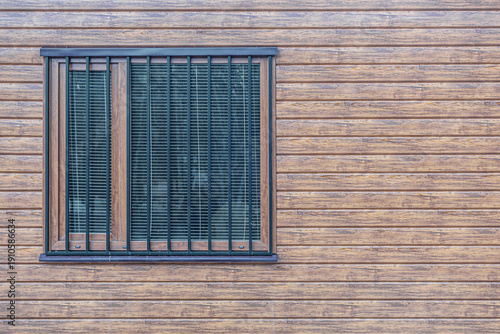 abstract background of window with metal security bars on a house facade clad in wood-look plastic panels, front view with horizontal siding texture close up