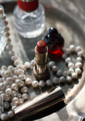 Luxury beauty flat lay: deep red perfume, gold lipstick, black case on iridescent mother-of-pearl tray with natural pearls. Soft dreamy lighting, romantic glow, feminine elegance 