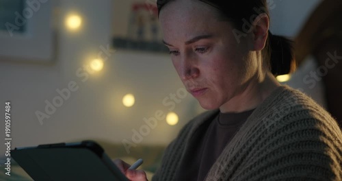Focused Woman Drawing on a Digital Tablet with a Stylus at Night