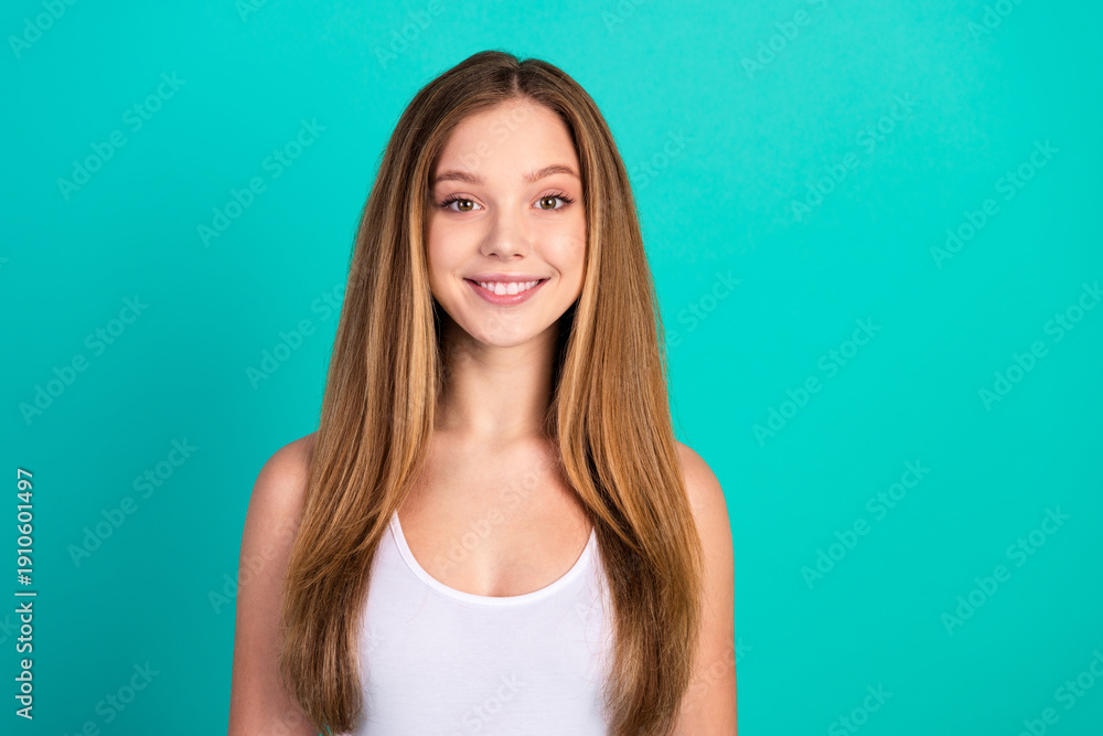 Fototapeta premium Portrait of a young woman smiling confidently against a vibrant turquoise background showcasing casual style