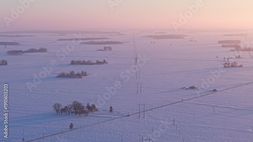 Electrical transmission lines extending across frozen winter plain, aerial backdrop at sunset