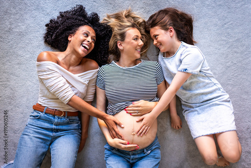 Friends and daughter touching pregnant belly bonding