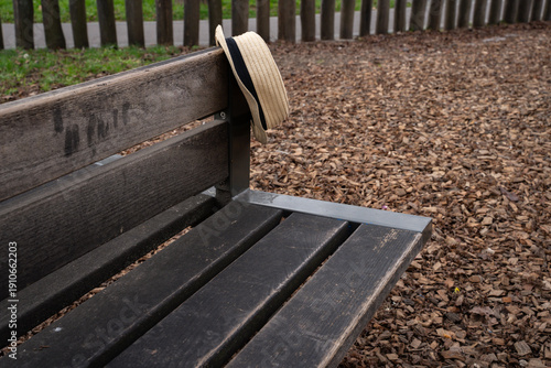 straw hipster summer hat on the back of a wooden park bench outdoors. Simple everyday scene showing a casual personal accessory placed in a public green space.