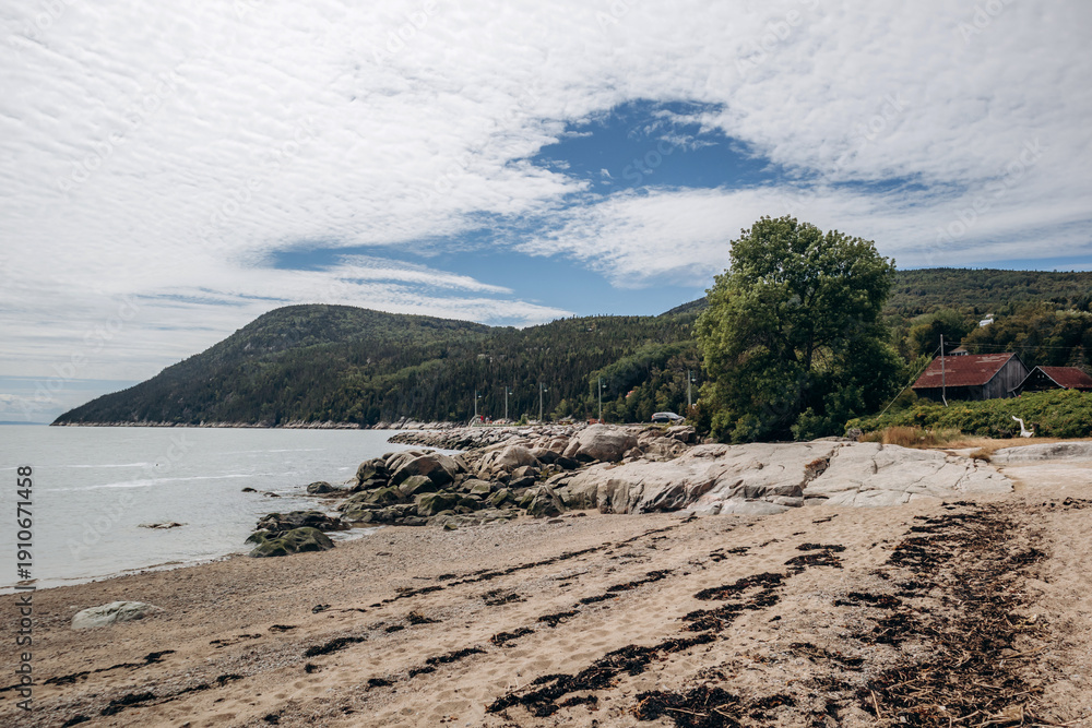 Obraz premium Sandy beach and rocky shoreline with gentle waves along the Saint Lawrence River in rural Quebec village, Port-au-Persil, Canada