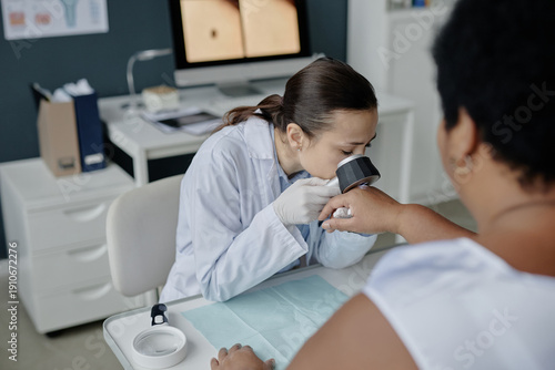 Quadro em tela Young adult Asian woman dermatologist examining hand of middle aged Black woman