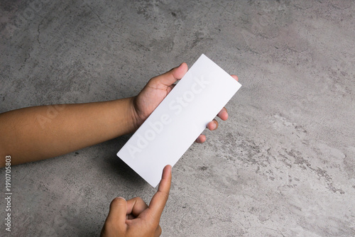 Hands holding blank white paper on a gray table, viewed from a 45-degree angle. Mockup for design.