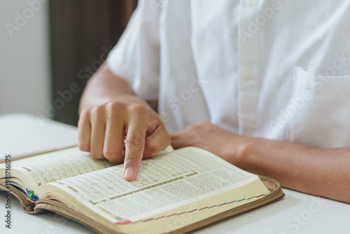 Man studying Islamic scripture with finger on page during Ramadan at home. Concept of faith, peace, devotion, spiritual growth, and Islamic education during the holy month of Ramadan
