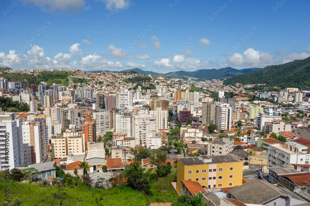 Fototapeta premium Skyscrapers and buildings in city nestled among green mountains. Pocos de Caldas, Minas Gerais, Brazil. Panoramic aerial view