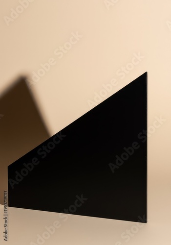 Composition of a sharp black geometric form against a light beige surface emphasizing shadow play and negative space ,isolation ,visual ,modern