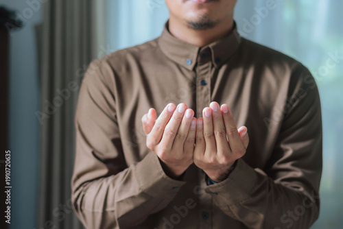 Muslim man holding cupped hands in prayer for Dua during Ramadan at home. Concept of faith, hope, peace, devotion, and gratitude during the holy month of Ramadan