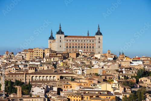 Obraz na płótnie The Alcázar of Toledo, a historic fortress and palace, stands prominently atop a hill overlooking the densely packed cityscape of Toledo, Spain, under a clear blue sky