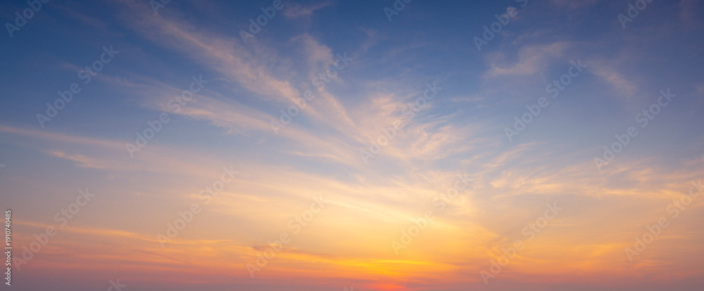 Fototapeta premium Dramatic sunset sky with orange and blue gradient clouds background,A beautiful panoramic view of the twilight sky during sunset, featuring soft wispy clouds illuminated by golden light against.