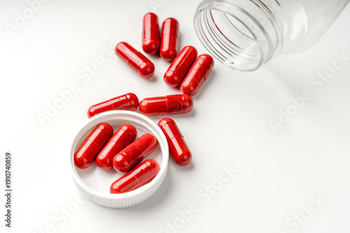Red capsules spilled from an open plastic container on a white background, photographed as a clean medical still life.


