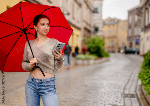 Young Woman With An Umbrella In The Old City Center Writes A Message On Phone