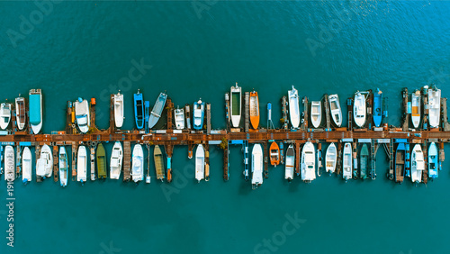 Aerial view of a long pier stretching into the teal river, adorned with an array of colorful boats basking under the summer sun, Sremska Mitrovica, Vojvodina, Serbia.