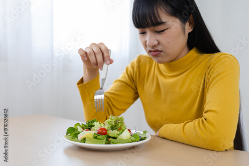 Canvas Print women frowning at salad holding fork at home, reluctant to eat healthy food