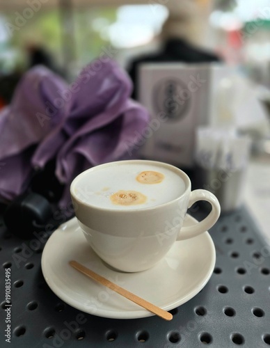 White cup of cappuccino with purple umbrella on the table of street cafe