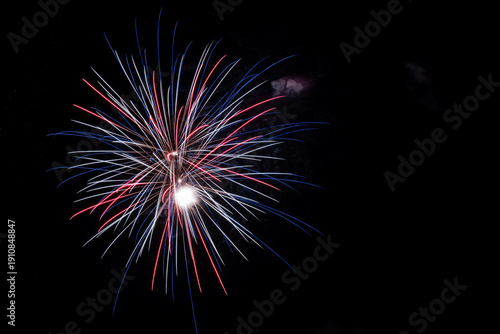 A brilliant patriotic firework explosion in vibrant red, white, and blue radiates in a chrysanthemum pattern with trailing sparks against a solid black night sky