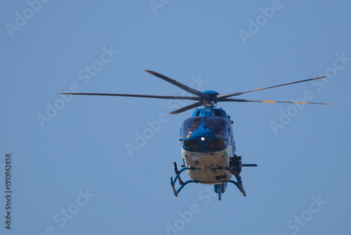 Blue and white helicopter inflight on patrol against clear blue sky. 
