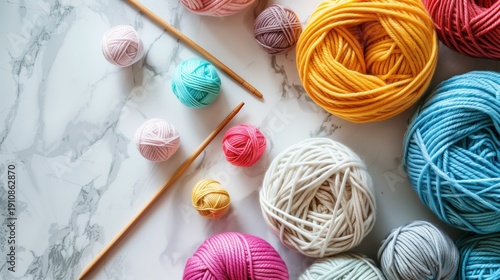 National Craft Month: Overhead flat lay of colorful hand-knitted items, wooden knitting needles, balls of merino wool yarn in pastel colors, crafting tools on white marble surface