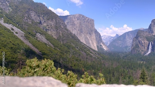 Yosemite valley panoramic view presenting towering granite cliffs of el capitan and distant half dome, with bridalveil fall tumbling into the evergreen forest below a summer sky