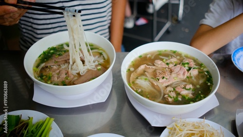 Fotografia People enjoying authentic vietnamese pho soup with beef and rice noodles, using