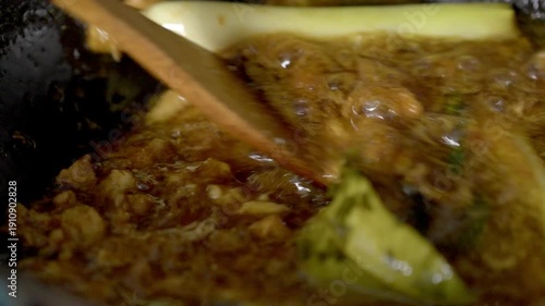 Glistening Savory Meat Stew Simmering in a Pot with Wooden Stirring Spatula