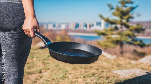 Woman holding empty black frying pan outdoors during sunny day. Cooking concept. Kitchenware for outdoor meal preparation and healthy food.