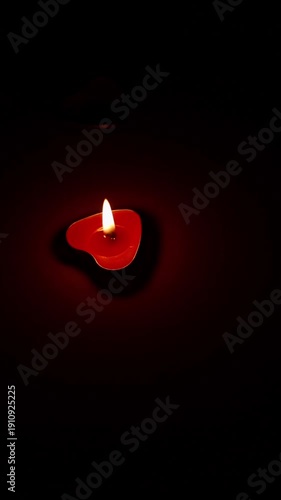 A single red heart-shaped tea light burns in the dark, the heart spinning calmly and the flame flickering with a warm light.