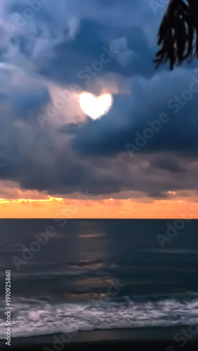 Heart shape appears in clouds over ocean during sunset near shore with waves crashing, creating a scene of natural beauty and connection