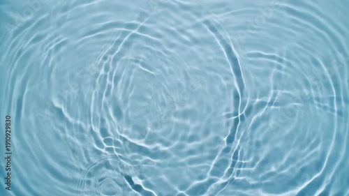  Top-down view of gentle water ripples forming circular patterns. Natural lighting and smooth motion create a relaxing visual.