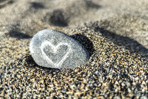 Rock with heart symbol resting on sand shows a simple expression of love and connection often found in romantic places or special moments by the beach. Concept of love and health