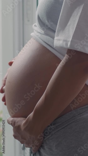Vertical Screen : Young Asian Pregnant couple hug and hold belly talk with their child. Mom and Dad happy smile peaceful while take care baby pregnancy near window in living room at home. Slow motion.