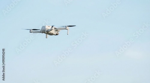 Modern grey unmanned aerial vehicle flies forward in a clear pale blue sky demonstrating aerial surveillance or photography capability.