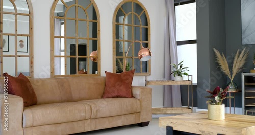 Camera is slowly panning right, revealing tan leather sofa, rust pillows, arched mirrors, window