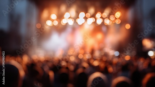 A blurred view of a large crowd at a concert, with warm, bright lights highlighting the stage.