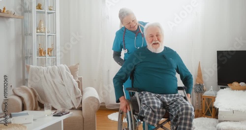 Nurse pushing retired senior man with disability in wheelchair at home, smiling and communicating warmly. Concept of mobility support, home care and compassionate healthcare.