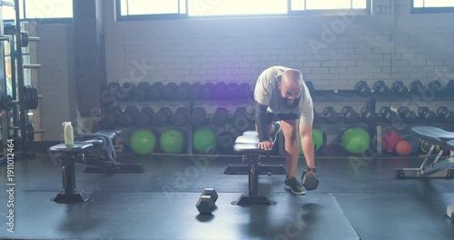 African American man at gym in shorts reaching for dumbbell bracing on bench pulling rows training