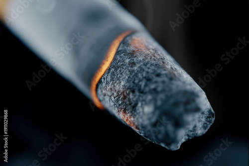 Burning cigarette creating smoke and embers on black background